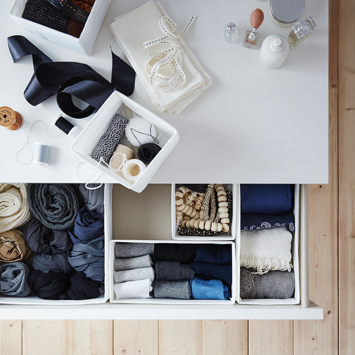 Petites boîtes SKUBB blanches pour vêtements et accessoires, sur le dessus et dans un tiroir ouvert d’une commode MALM blanche.