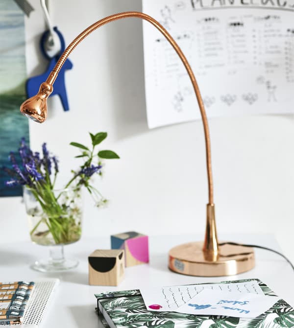 Pezzo di scrivania arredata con una lampada di rame, fiori e oggetti.