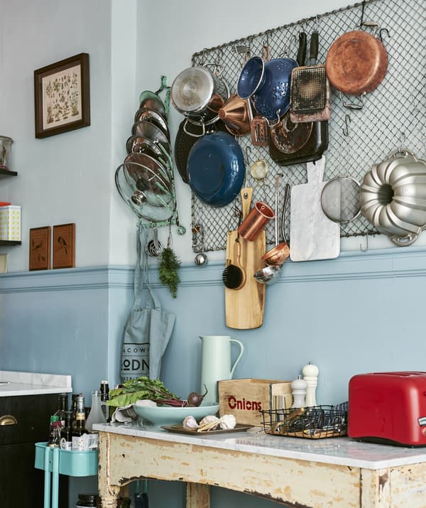 Photo de casseroles, poêles et ustensiles de cuisson suspendus à une grande grille au mur de la cuisine, au-dessus d'une table basse rustique.