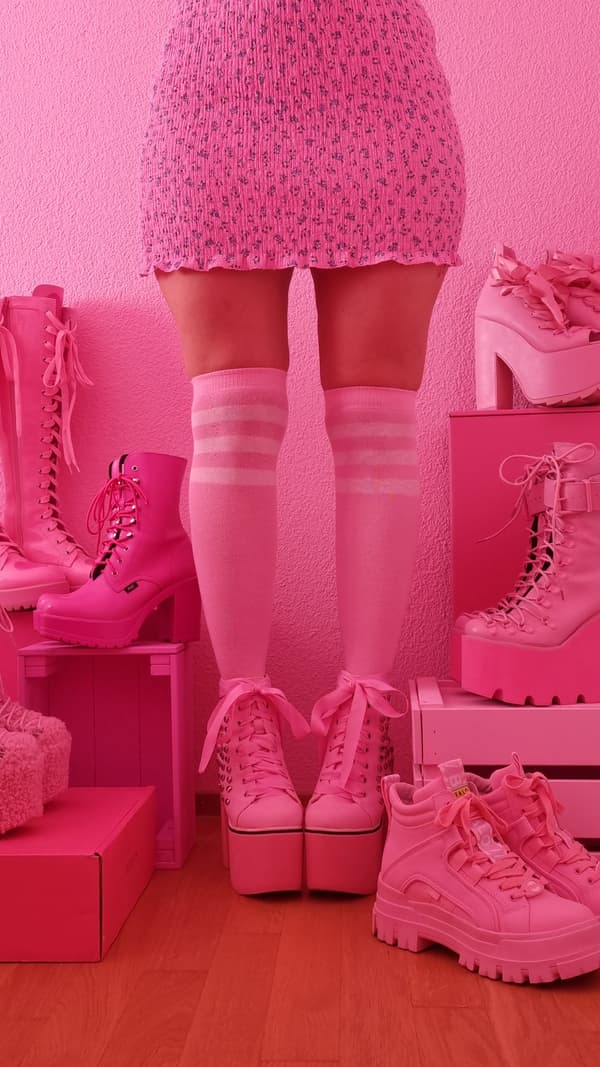 Photo des jambes d’une femme portant une jupe rose, des chaussettes roses montant jusqu’aux genoux et des chaussures roses, entourée d’autres chaussures roses.