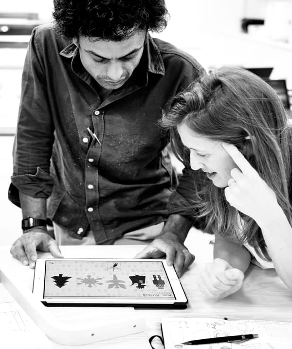 Photo en noir et blanc montrant une femme et un homme penchés sur une tablette numérique, examinant les illustrations affichées.
