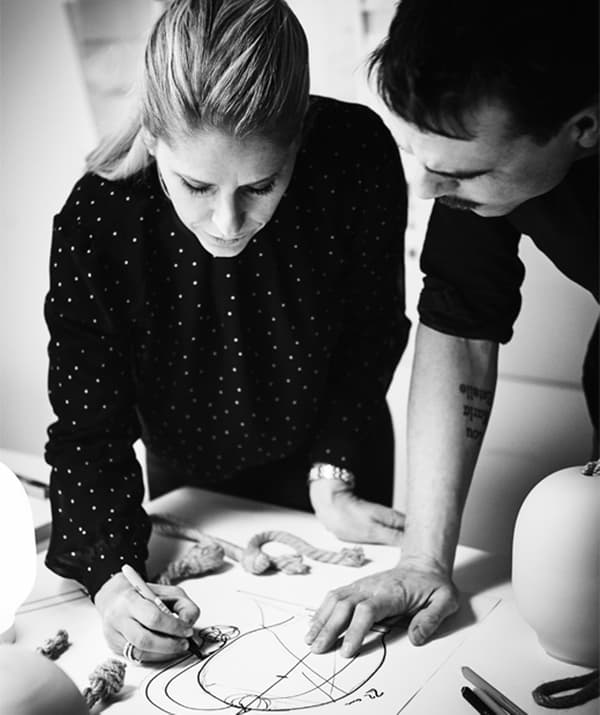 Photo en noir et blanc montrant une femme et un homme penchés au-dessus d’une table, concentrés sur un croquis que la femme dessine.