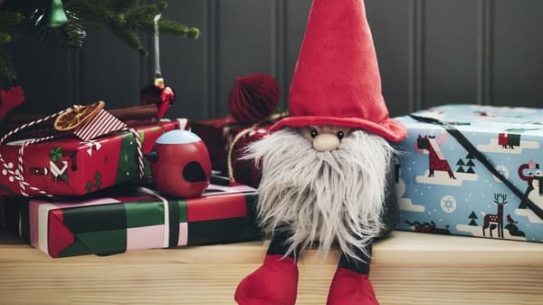 Photo of a Santa gnome decorative soft toy sitting by a Christmas tree surrounded by gifts