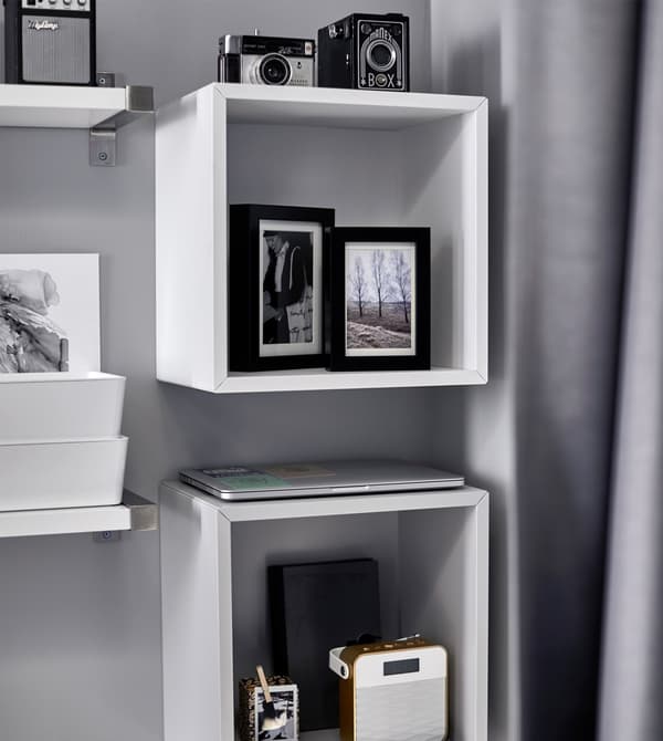 Photos, cameras, and a stereo are displayed on a shelf above a bed.