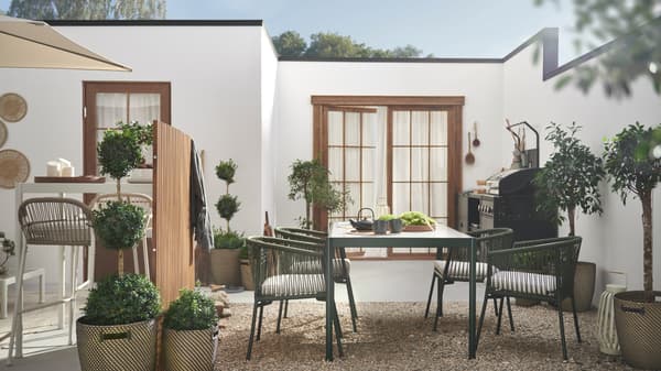Piante verdi e mobili da giardino in un luminoso e spazioso patio chiuso con pavimentazione in ghiaia e pietre vicino a un edificio bianco a un piano - IKEA.