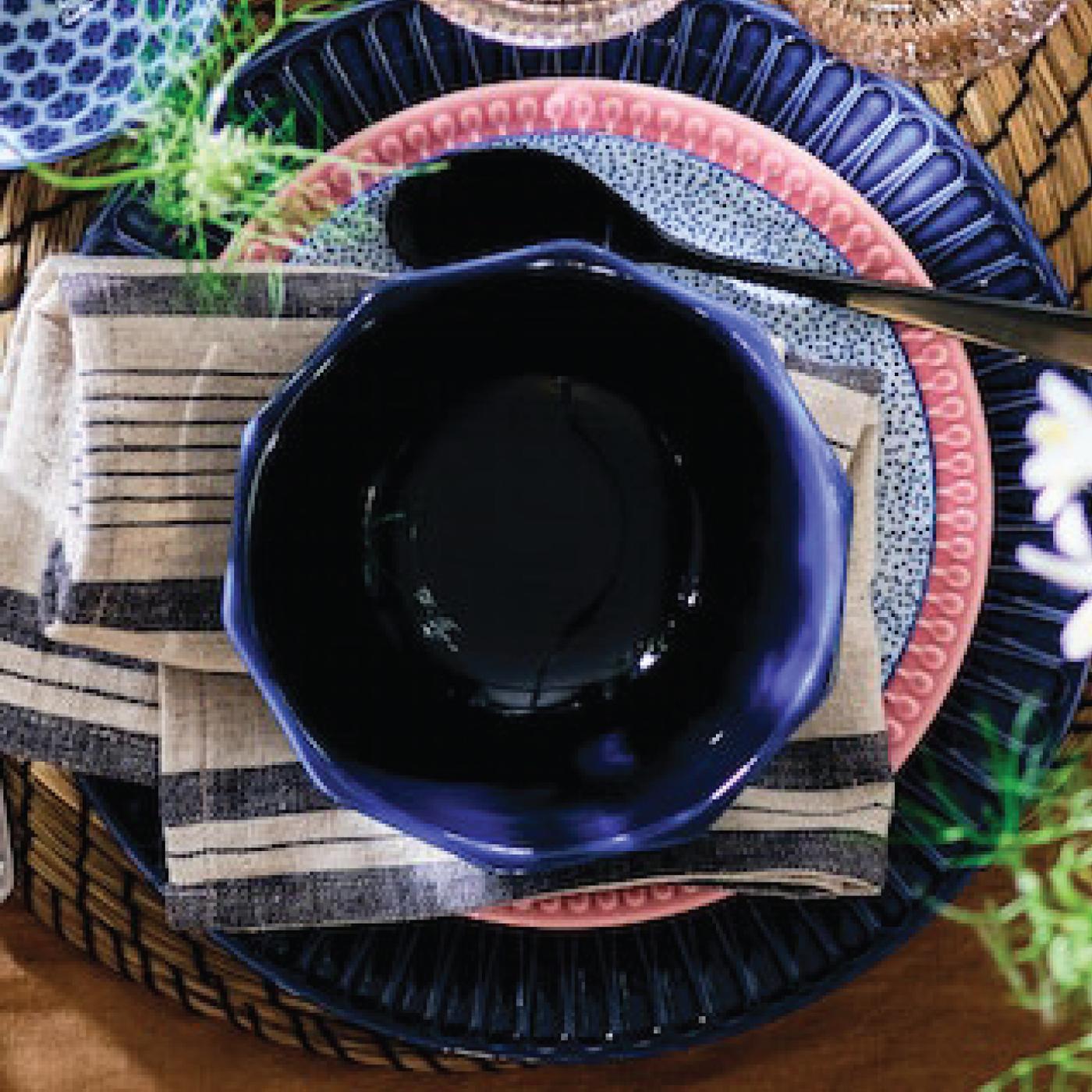 Piatto da portata blu su piatto piano multicolore e ciotola blu e posate nere con tovaglioli blu e bianchi