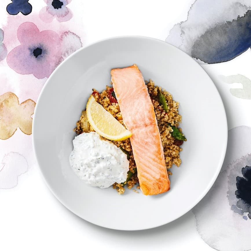 Piatto piano bianco con salmone e farro su tovaglia fantasia multicolore