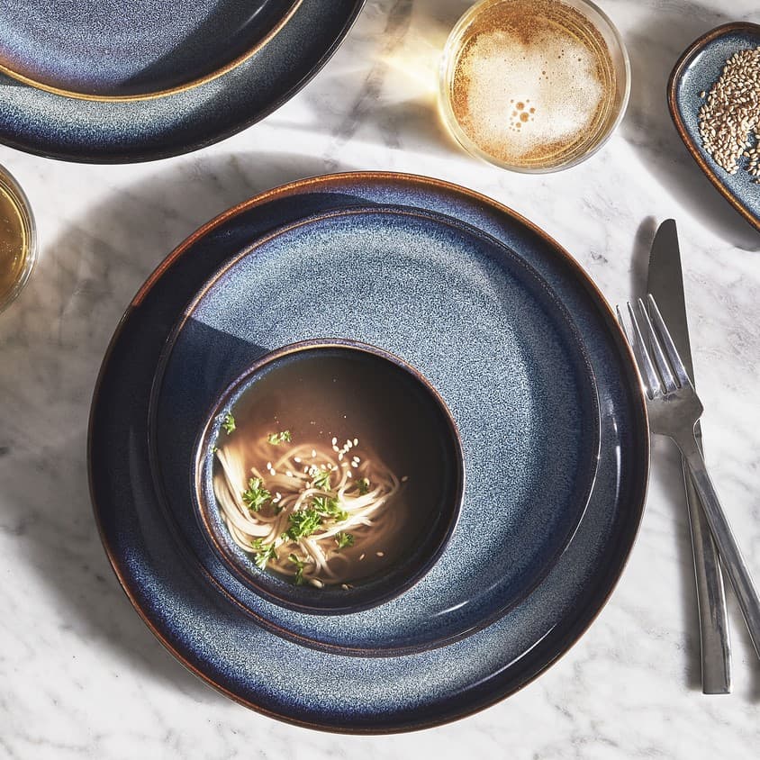 Piatto piano grigio chiaro con sopra posate inox e tovagliolo beige su tovaglietta naturale