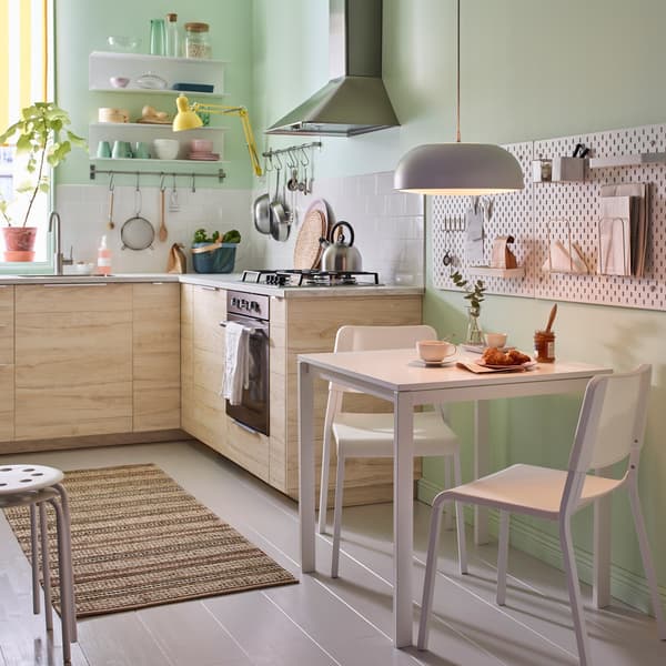 Piccola cucina beige, verde e bianca con tavolo MELLTORP bianco e due sedie impilabili TEODORES – IKEA