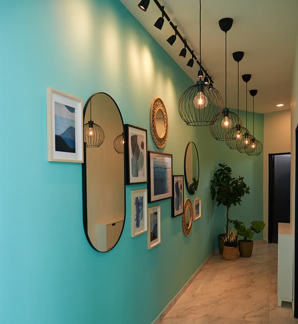 Picture frames and a mirror is hung on a turqoise wall.