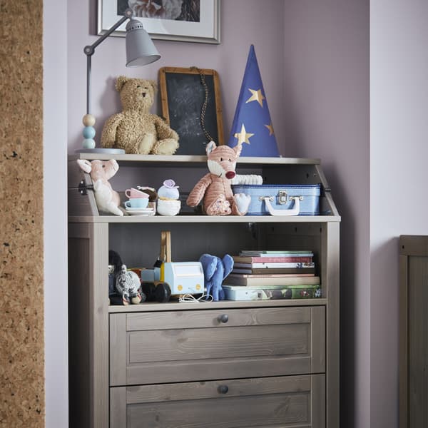 Picture of a changing table unit/chest of drawers with toys and books on it.