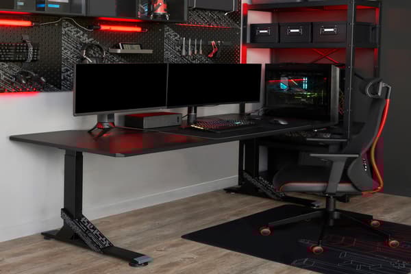 Picture of a desk with two screens and a red and black gaming chair in front of it.