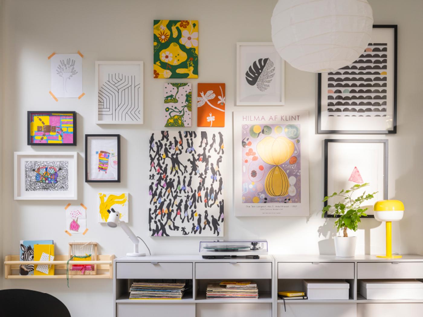 Pièce lumineuse avec une rangée de buffets SPIKSMED gris clair devant un mur blanc couvert de nombreuses affiches et œuvres artistiques encadrées.