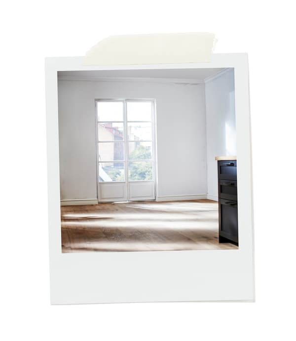 Pièce vide baignée de soleil avec plancher en bois et murs blancs, dotée d’une double porte-fenêtre donnant sur un jardin.