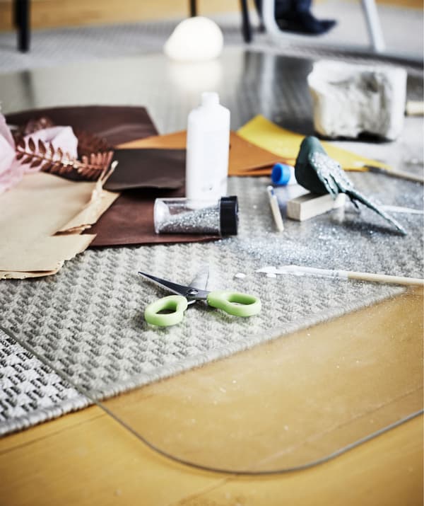 Pieces of paper and painting and art supplies strewn across a floor protector, protecting the carpet from damage.