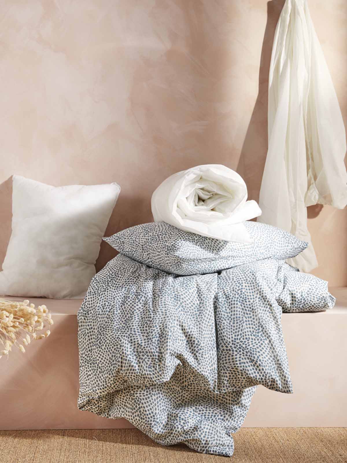 Pillows and cushions in various colours are stacked on top of one another on a bed.