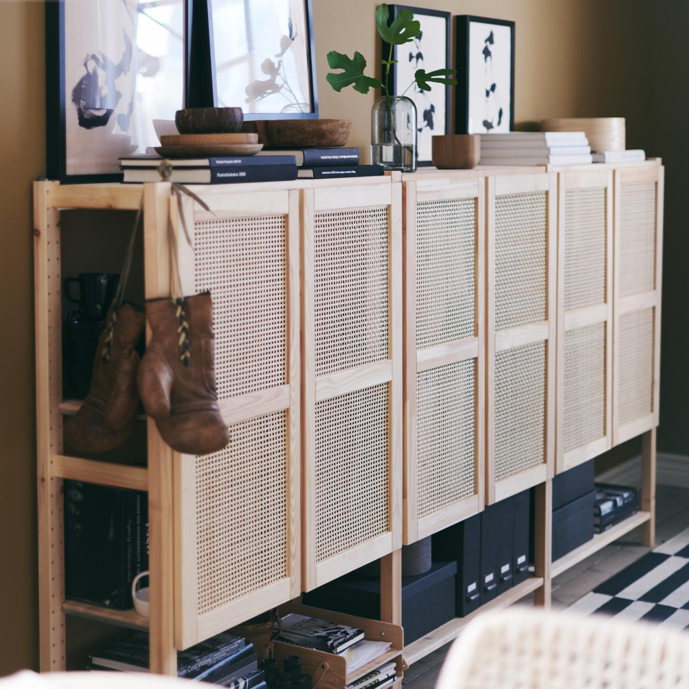 Pine IVAR shelving units with doors against a wall, with art, books, bowls and a plant above, and a pair of boxing gloves.