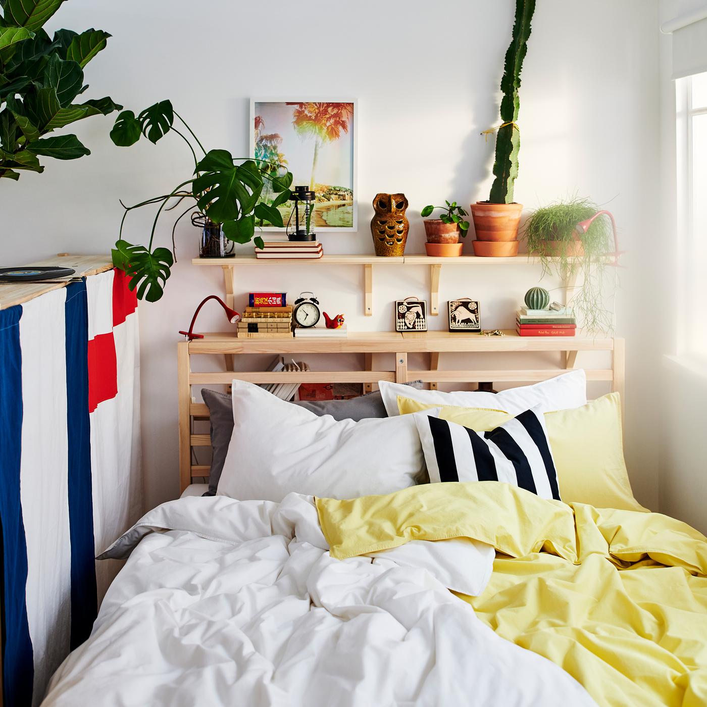 Pine, TARVA bed frame dressed with white and pale yellow ÄNGSLILJA bed textiles, against a white wall with aspen shelves.