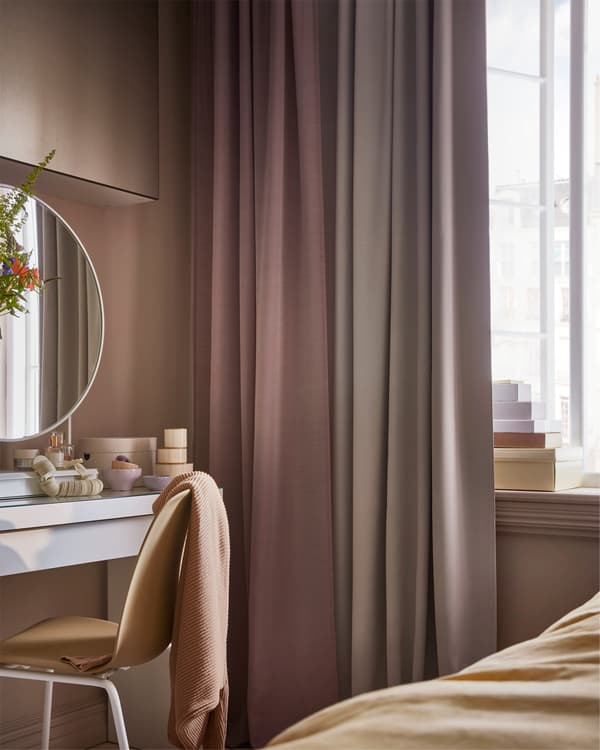 Pink and gray curtains, a yellow chair, and white dressing table with a white table mirror and small boxes standing on it.