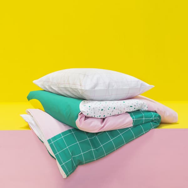 Pink and green patterned bedding folded up on a pink and yellow shelf.