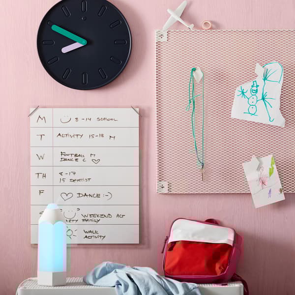 Pink wall with noticeboard, whiteboard and clock.
