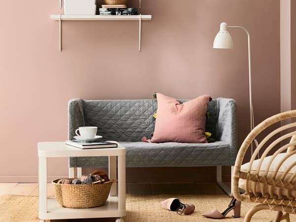 ピンクの壁にグレーのソファを合わせたシンプルなリビング。ラタンチェアと白いテーブルがアクセント。
