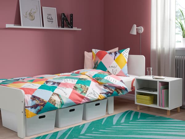 ピンクの壁に白い収納付きベッドを置いた子ども部屋。幾何学柄の寝具でポップな雰囲気。