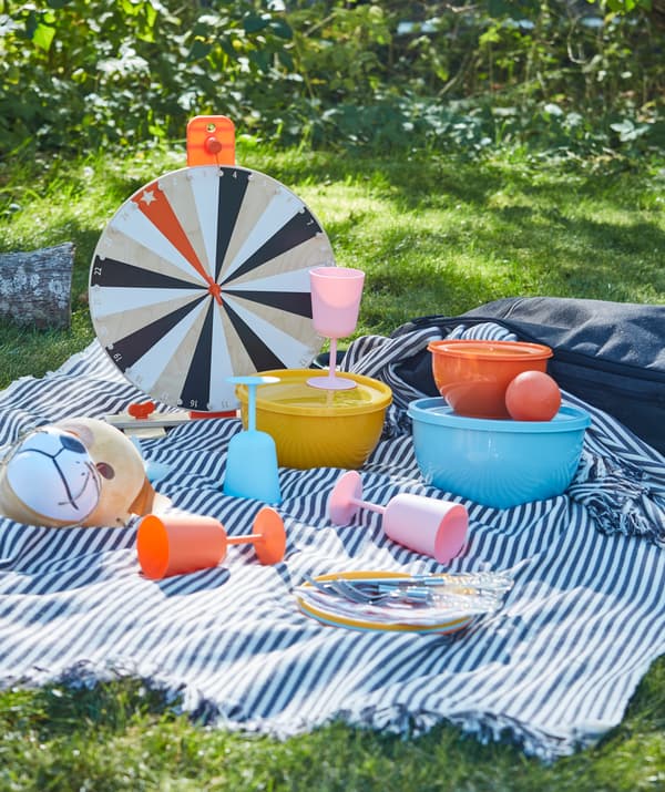 Pique-nique sur l’herbe avec vaisselle en plastique et verres à vin de différentes couleurs.