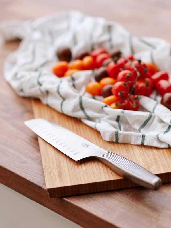 Pisau sayur keluli tahan karat di atas landas cencang kayu di sebelah tomato di atas tuala pengesat.