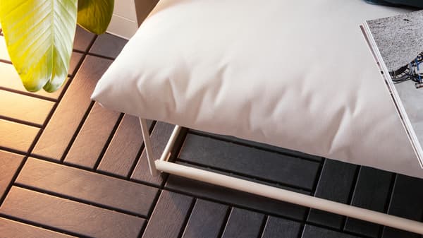 Piso de exterior imitación madera por tramos, debajo de un sofá de exterior tapizado en blanco y un libro encima.
