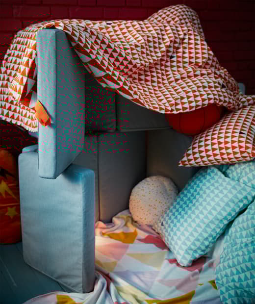 Placez des matelas SLÄKT sur le côté, ajoutez une couette sur le dessus, et voilà un fort ! Ajoutez un fauteuil poire moelleux pour le confort, mais aussi pour solidifier la construction. 