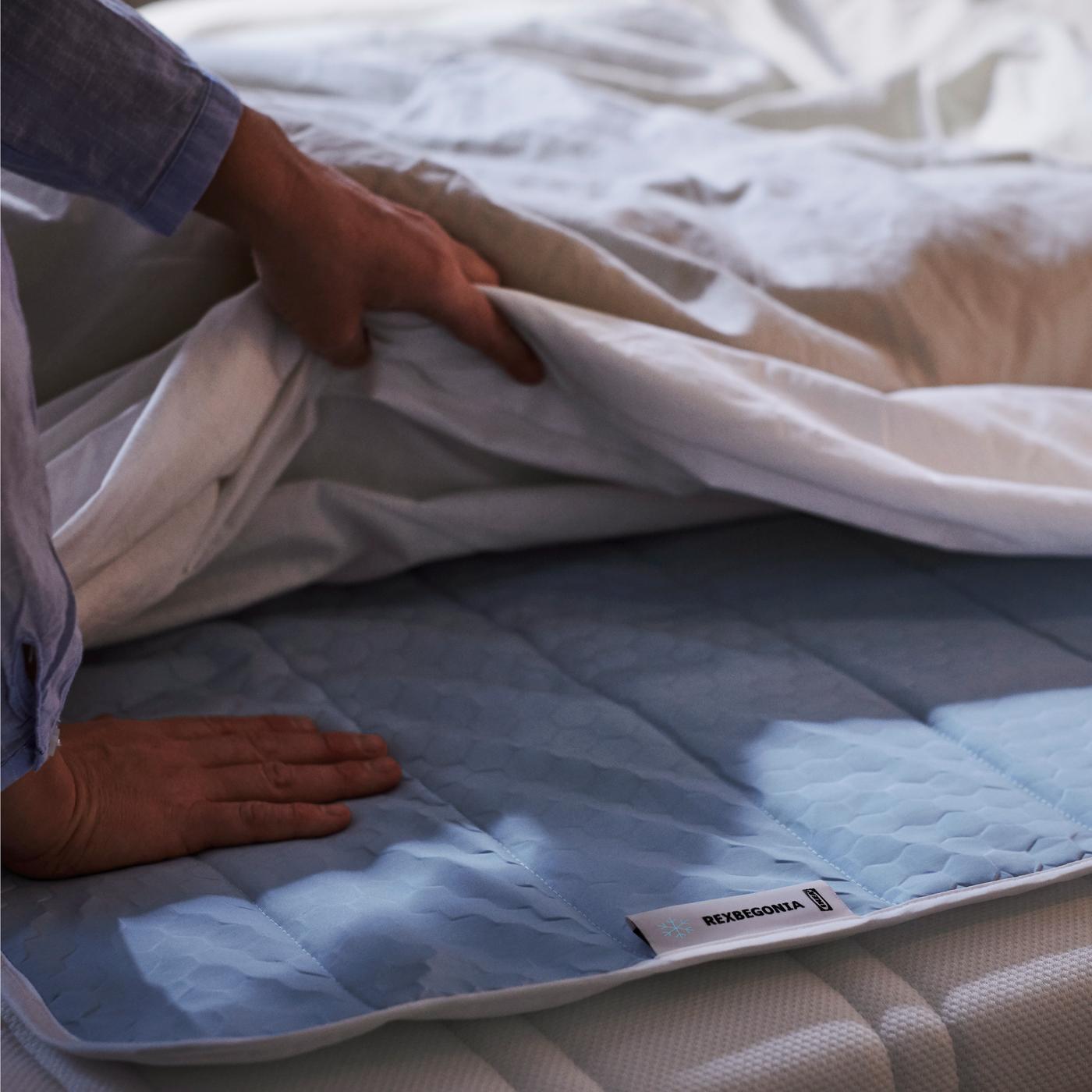 Placing a blue quilted mattress protector on a bed