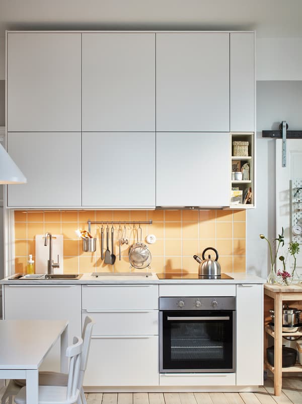 Plan de travail de cuisine avec évier, table de cuisson et ustensiles, encadré de rangées d’armoires dotées de façades METOD en blanc.