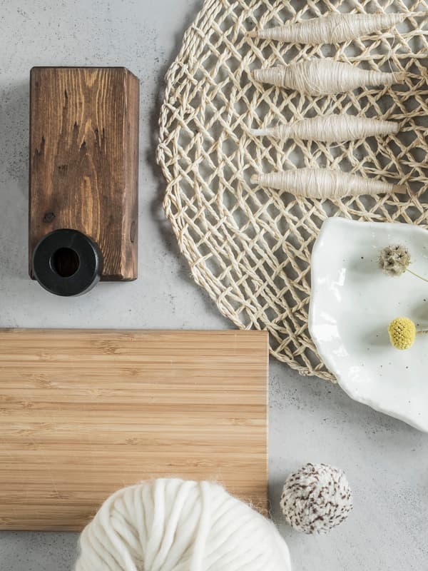 Planche à découper en bambou APTITLIG sur une surface en marbre blanc, près d’un set de table grossièrement tissé et de quatre fuseaux de fil.