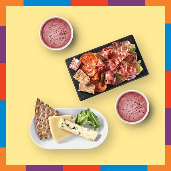 Planche en ardoise rectangulaire contenant de la charcuterie à côté de deux ramequins blancs contenant une boisson rose et d'un d'une assiette ovale contenant des morceau de fromage et tranche de pain de seigle et un peu de salade , détourés sur fond jaune pâle avec bordure de couleurs rouge, bleu, violet, orange et vert.