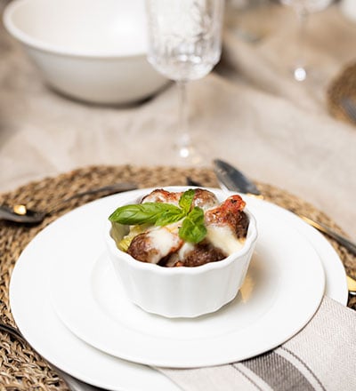 Plant ball gratin in white dish, topped with melted cheese and fresh basil leaves