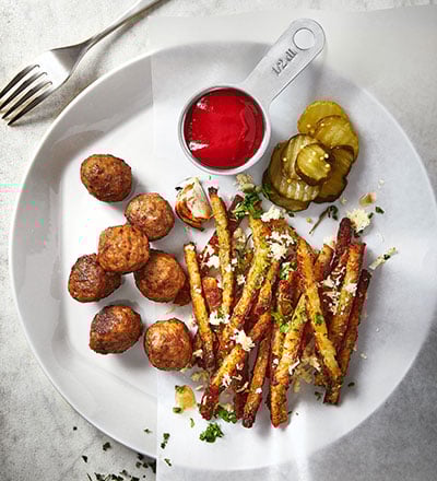 Plant balls with fries, ketchup, pickled cucumber served on white dish