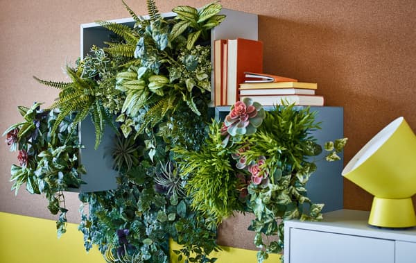 Plantas verdes artificiales en maceteros usadas para crear decoración de pared en cajas de almacenaje abierto.