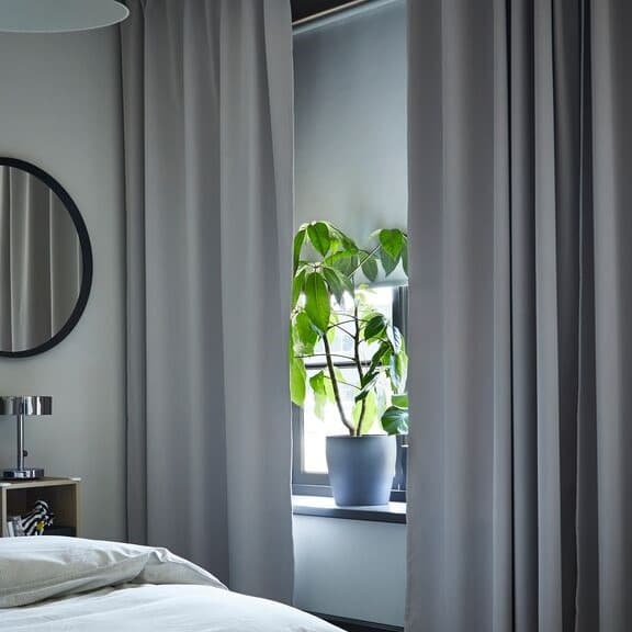 Plante verte dans un pot sur le bord d'une fenêtre entourée de rideaux gris dans une chambre
