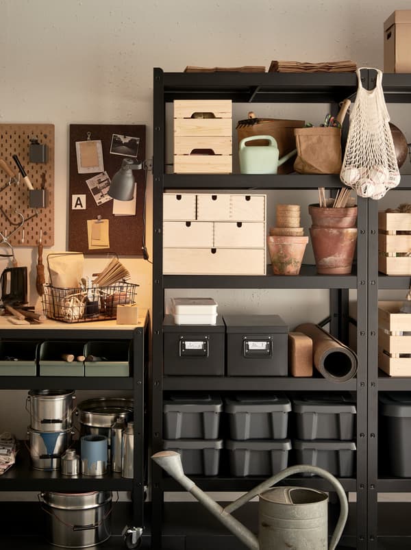 Plastic and wooden boxes, cardboard boxes and baskets made from textile inside BROR shelving unit organising a garage wall.