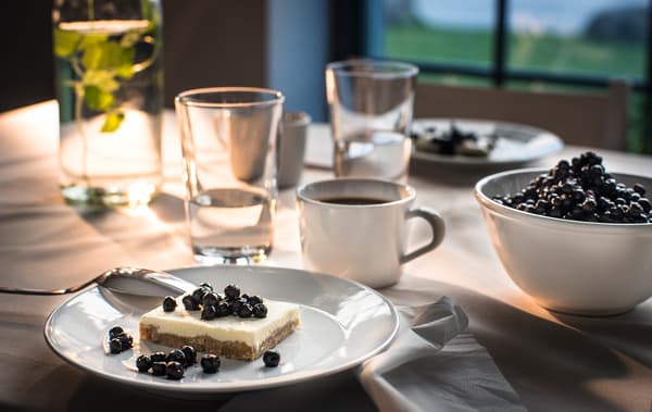 Plat de postres amb un pastís de fruites del bosc a una taula amb cafè i la resta de la vaixella.