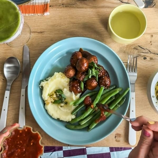 Plate of mashed potatoes, green beans and glazed meatballs with sauce on a wooden table.