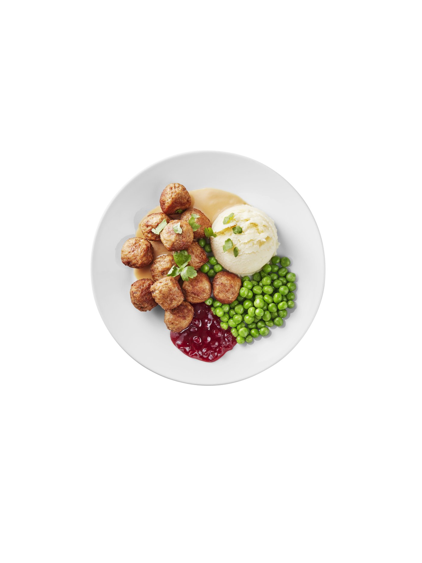 Plate of Swedish meatballs served with mashed potatoes, green peas, lingonberry sauce, and creamy gravy.