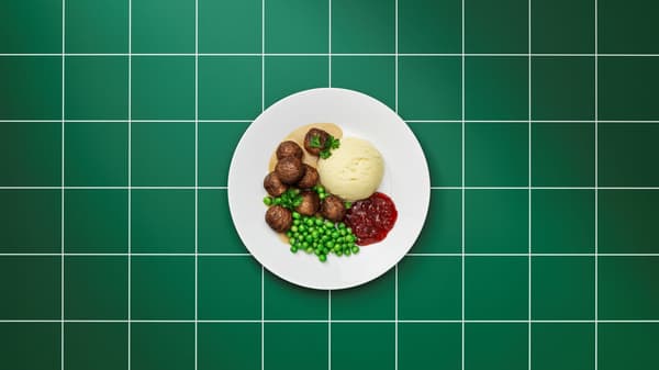 Plate of Swedish-style meatballs served with mashed potatoes, green peas, cream gravy, and lingonberry sauce, photographed from above on a green tiled background.