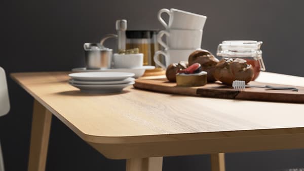 Plateau de table LISABO plaqué frêne, sur lequel sont disposés des tasses à café, une planche à découper, un pot de miel et des petits pains.