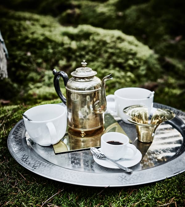 Plateau en métal avec tasses, café et bouilloire, posé par terre dans un coin détente aménagé pour une fête de noces en forêt