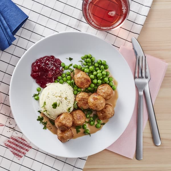 Plato con albóndigas, puré de patatas, guisantes y un poco de mermelada servida en un plato blanco.