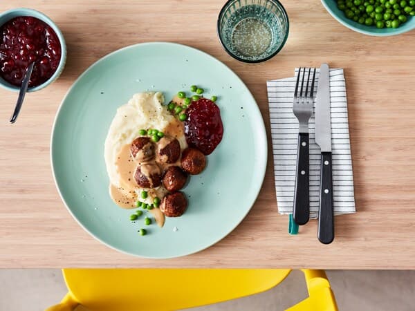 Plato de albóndigas con pure y arvejas sobre una mesa de madera, en un plato celeste redondo.