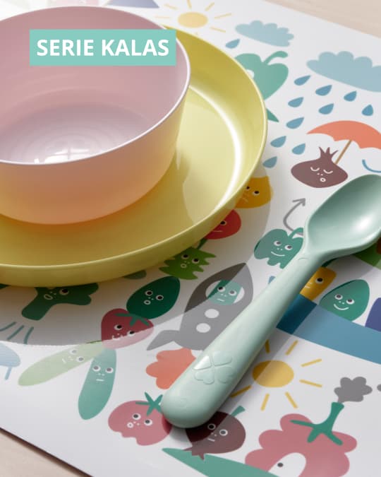 Platos de plástico de colores de la serie KALAS sobre una mesa con una cuchara plástica al costado.