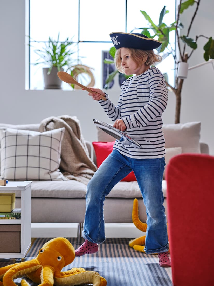 Play
Child dressed as a sailor playing with a wooden toy steering wheel in a bright, playful room with stuffed toys.